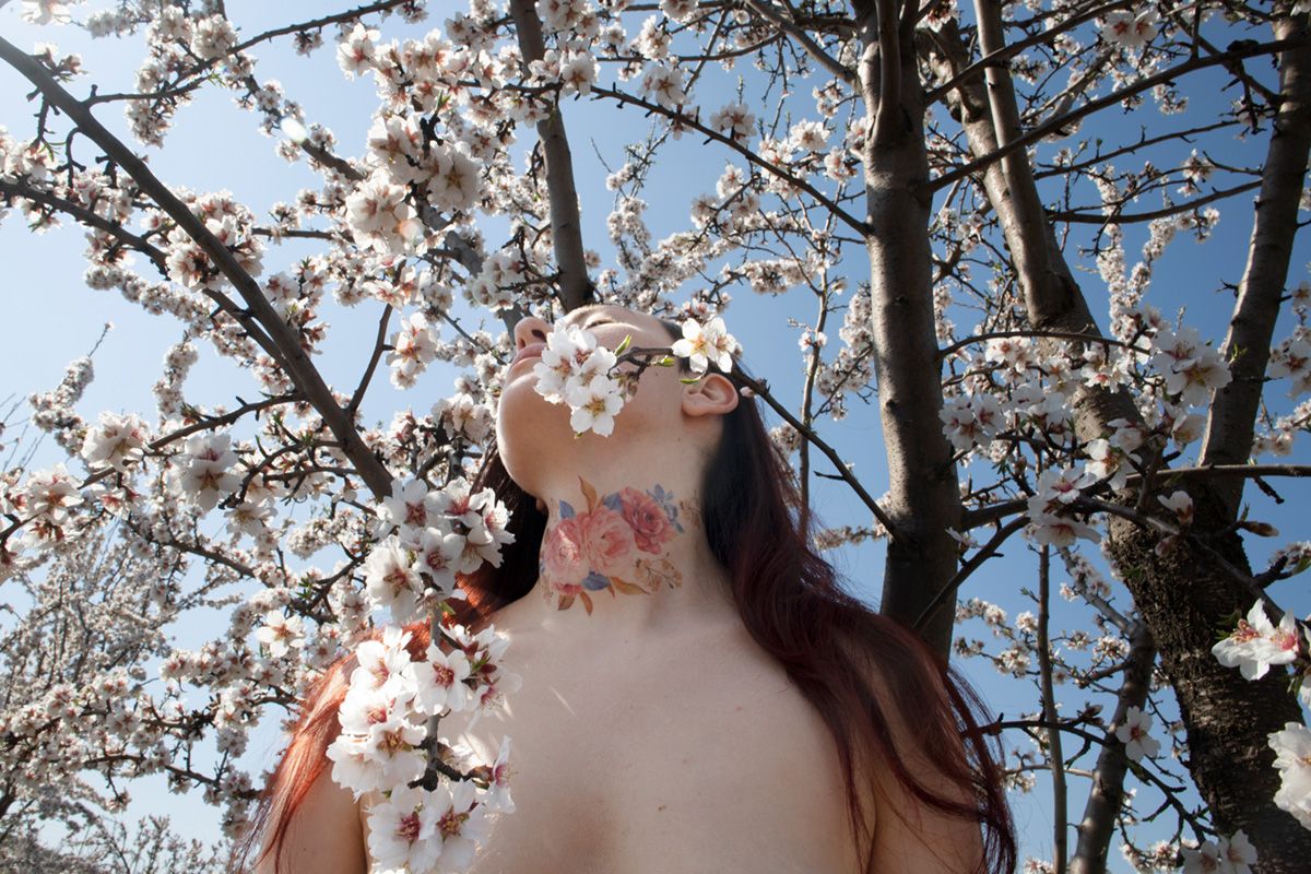 Imagen de autorretrato de la artista fotográfica Alba Mozas Gómez que posa un retrato entre flores de almendro antes de empezar la pandemia en busca de la libertad y el contacto con la naturaleza, obra para la exposición de Photo España, encuentros en tiempo presente, festival internacional de arte y consagrado en el panorama Español